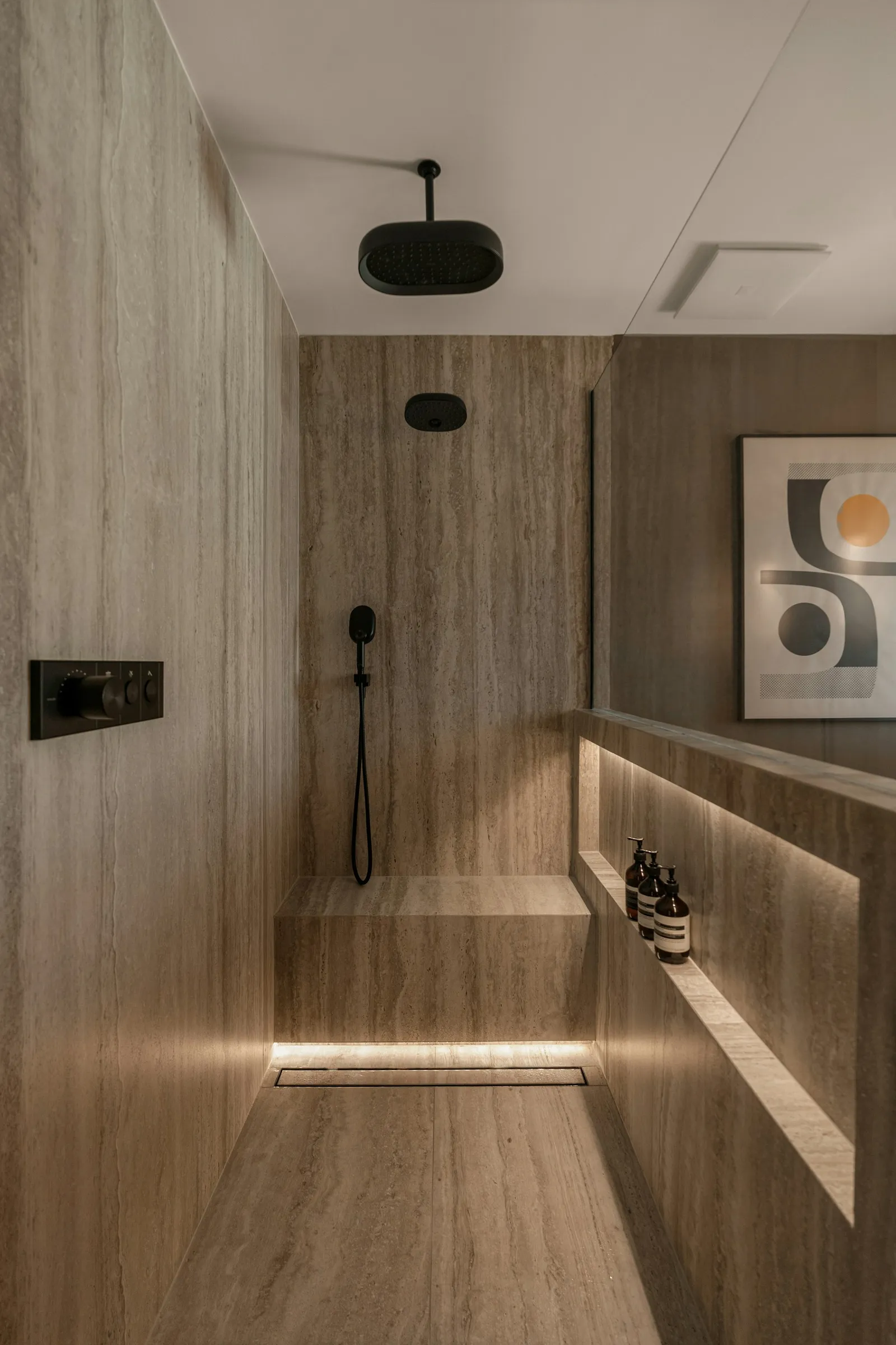 Natural stone surfaces, a precise shower niche, and understated black fixtures in a contemporary bathroom.