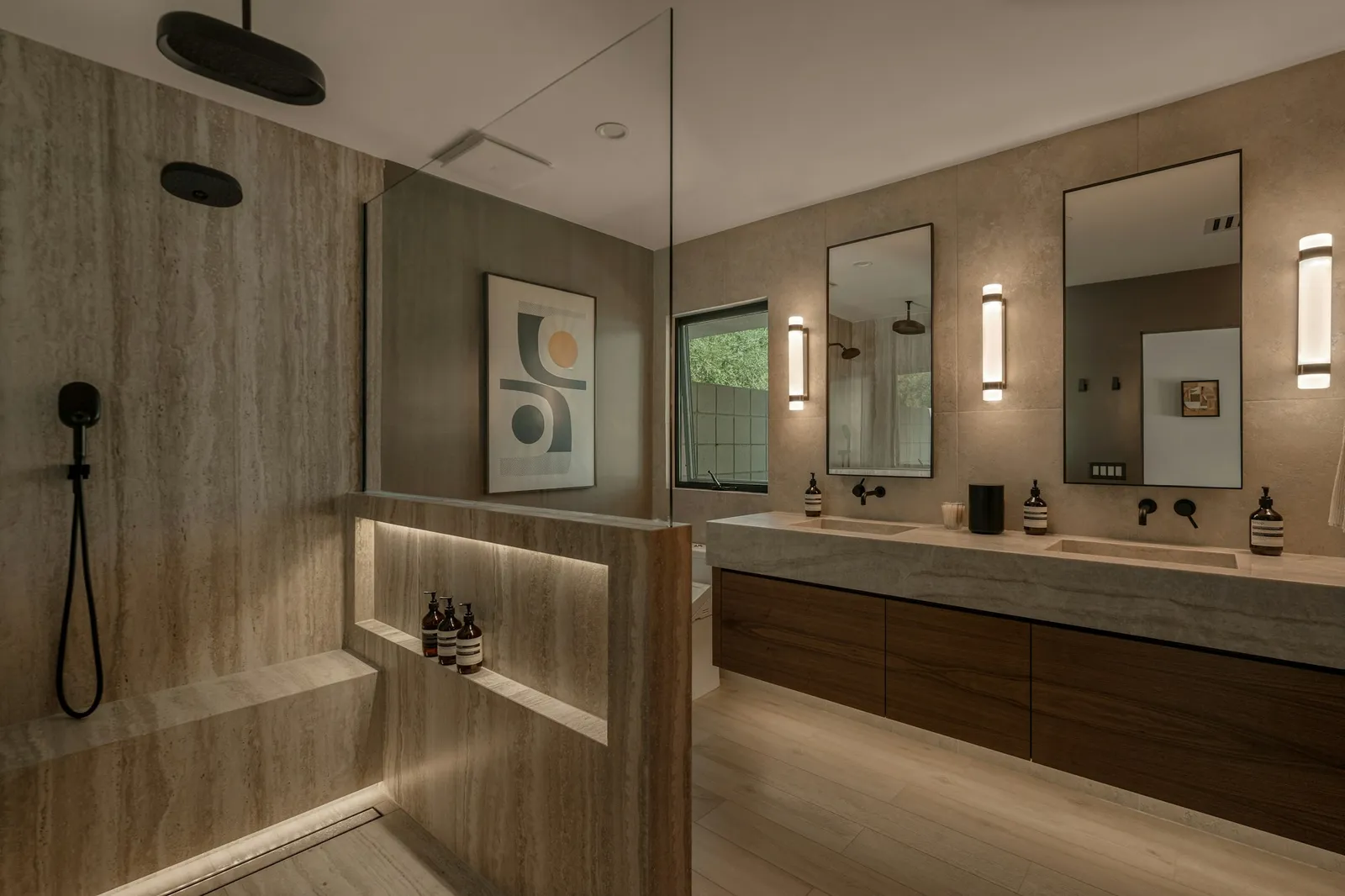A stone bathroom with a glass shower, floating wood double vanity, and softly lit mirrors.