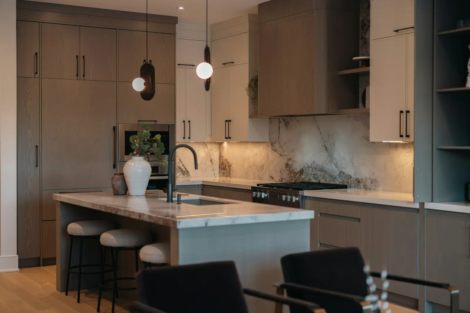 Wood cabinetry, a pale stone island, and warm pendant lighting in a contemporary kitchen.